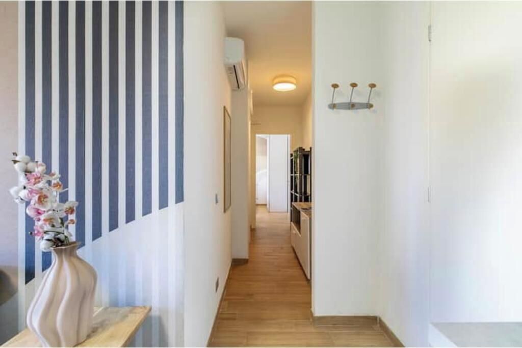 A hallway with striped wallpaper, a vase with flowers, and a light fixture on the wall.