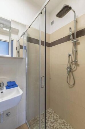 Un baño con ducha envuelta en vidrio, un lavabo y un espejo.