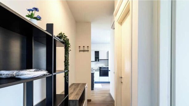 A narrow hallway with black shelving units, a wooden bench, and a plant. - Wallpaper Suites – 2 Bedrooms, 2 Bathrooms, and a Small Balcony (Padova)