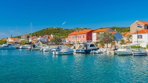 A coastal town with boats docked along the waterfront, buildings with red roofs, and a clear blue sky.