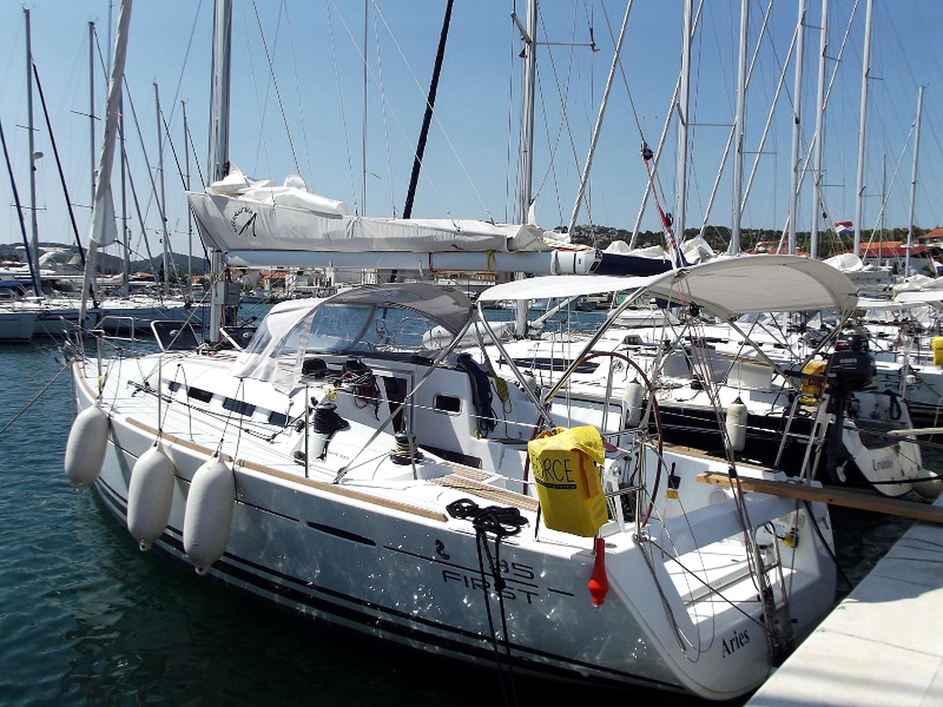 Un port de plaisance où sont amarrés de nombreux voiliers, avec une cabine dotée d’une terrasse couverte et d’une bouée de sauvetage fixée à proximité.