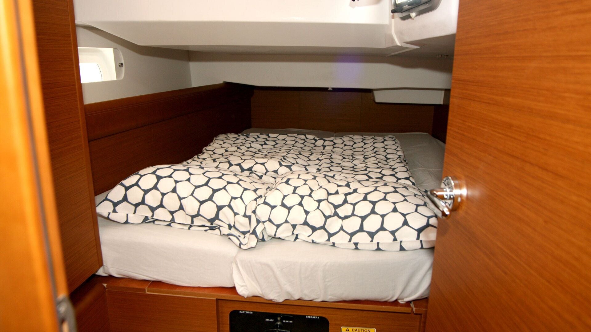 A compact bed with a patterned bedspread and a white pillow in a small room with wooden walls and a ceiling light.