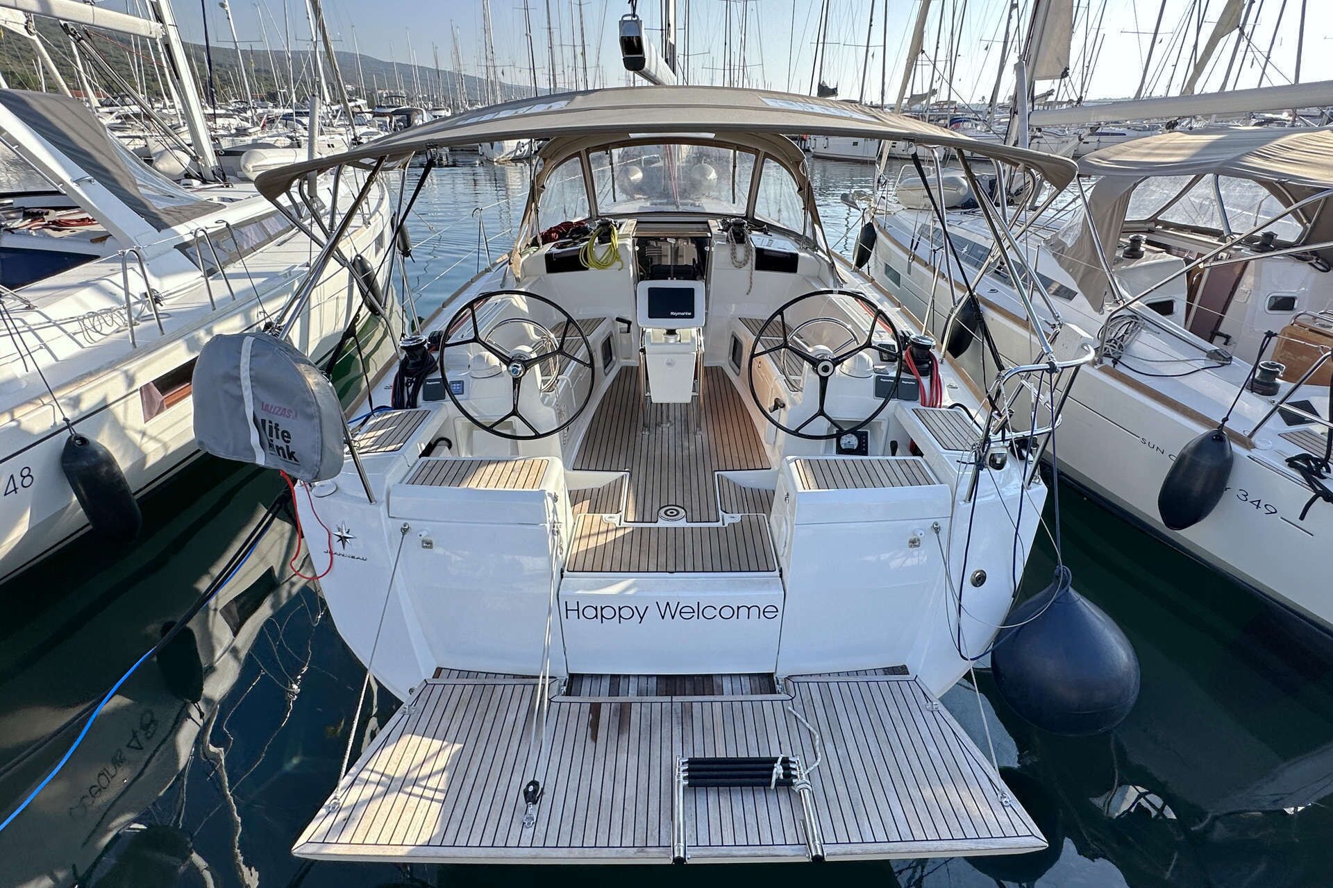 A yacht's deck with a 'Happy Welcome' sign, a steering wheel, and a control panel.