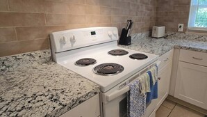 A kitchen with a white stove, granite countertops, and beige tiled walls.