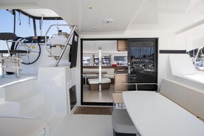 A yacht interior with a dining area, a seating area, and a view of the marina.