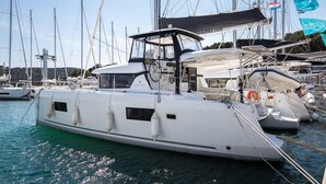 En vit lyxyacht låg förtöjd vid en hamn med flera master och flaggor, bland annat en blå flagga med texten ”BENETTO” och en röd- och vitrandig flagga.