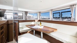 En lyxig inredning i en yacht med ett träbord, vita, bekväma sittplatser och stora fönster som ger utsikt över hamnen.