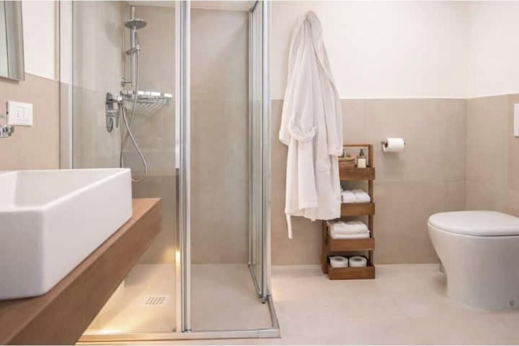 A modern bathroom with a glass shower enclosure, a white sink, and a wooden towel rack.