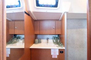 A compact bathroom with wooden cabinets, a sink, and a window with a warning label. - Sibenik Sun-soaked Sailing: A Luxurious Croatian Voyage (Pirovac)