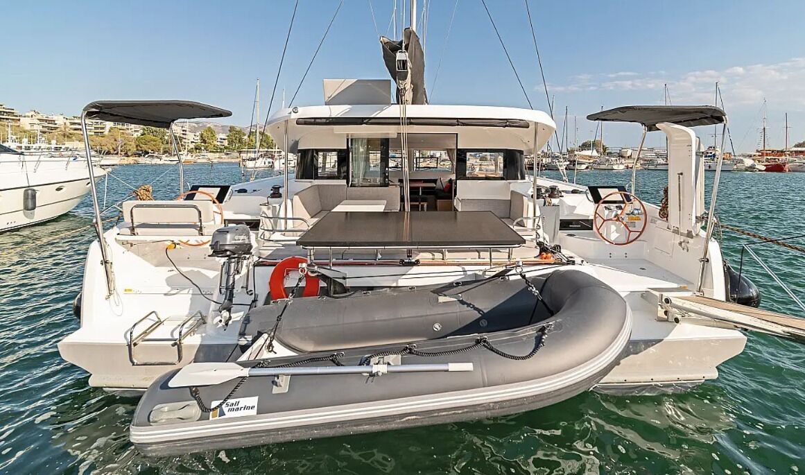 Un velero con zona de estar cubierta, timón y un pequeño bote inflable.