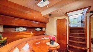 En lyxig inredning i en yacht med en böjd sittgrupp, ett litet bord med en vas, en trätrappa och ett runt fönster.