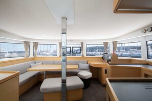 A yacht interior with a seating area, a control panel, and windows with a marina view.