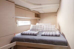 A compact bed with a quilted cover and two pillows, a small window, and a light fixture above the window. - Sun-Kissed Sailing Adventure in the Dodecanese Islands (Kos)