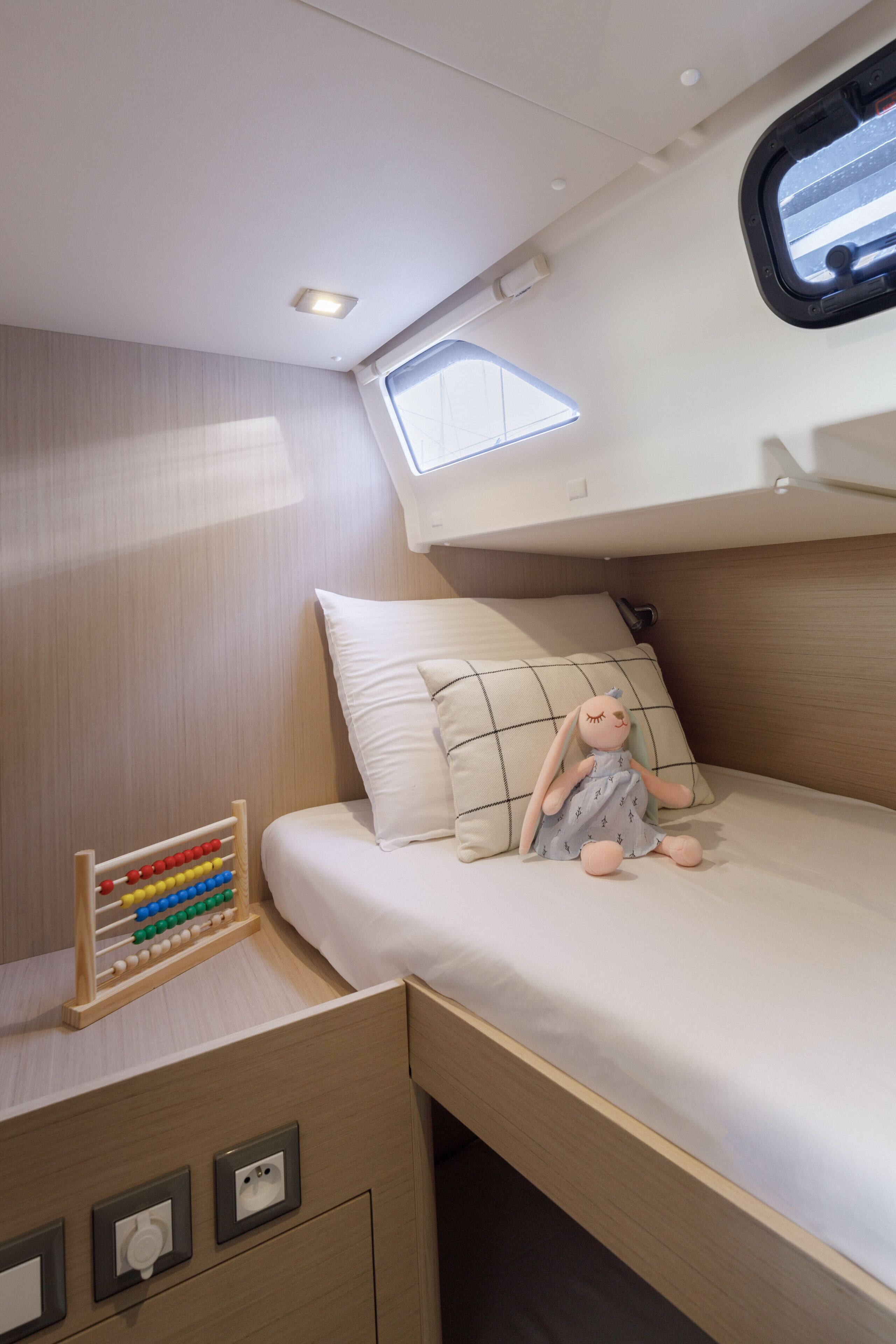 Een stapelbed met een klein raam, een nachtkastje met een rekenklem en een pluche speelgoed op het bed.