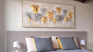 Quarto com cama, almofadas e uma obra de arte na parede.