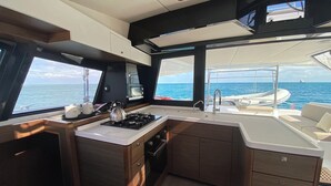 A compact galley with a stove, sink, and storage cabinets, overlooking the sea.
