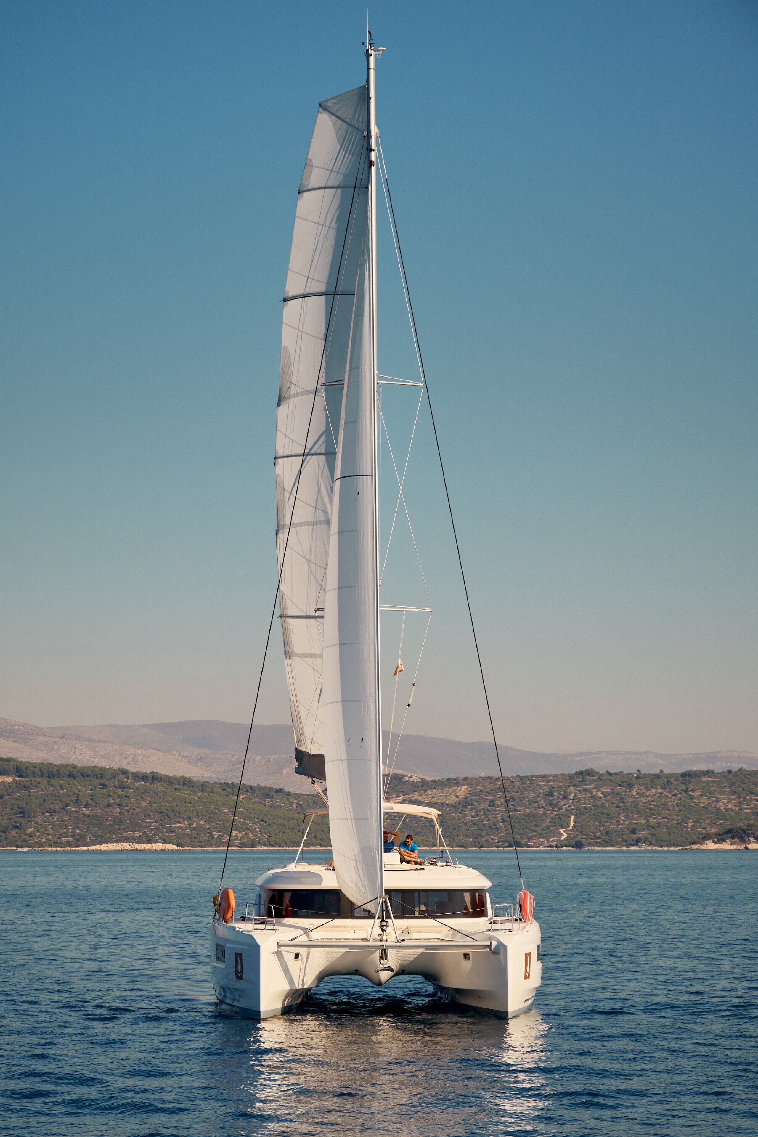 Un catamaran blanc à un seul mât naviguant sur des eaux calmes.