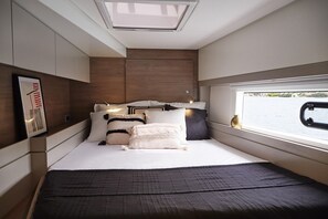 A compact bedroom with a skylight, a bed with multiple pillows, a bedside table, and a window with a view of the water. - Sun-Kissed Sailing Adventure in the Dodecanese Islands (Rodos)