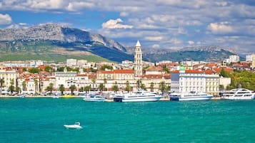 A coastal cityscape with a prominent tower, boats, and a mountainous backdrop.