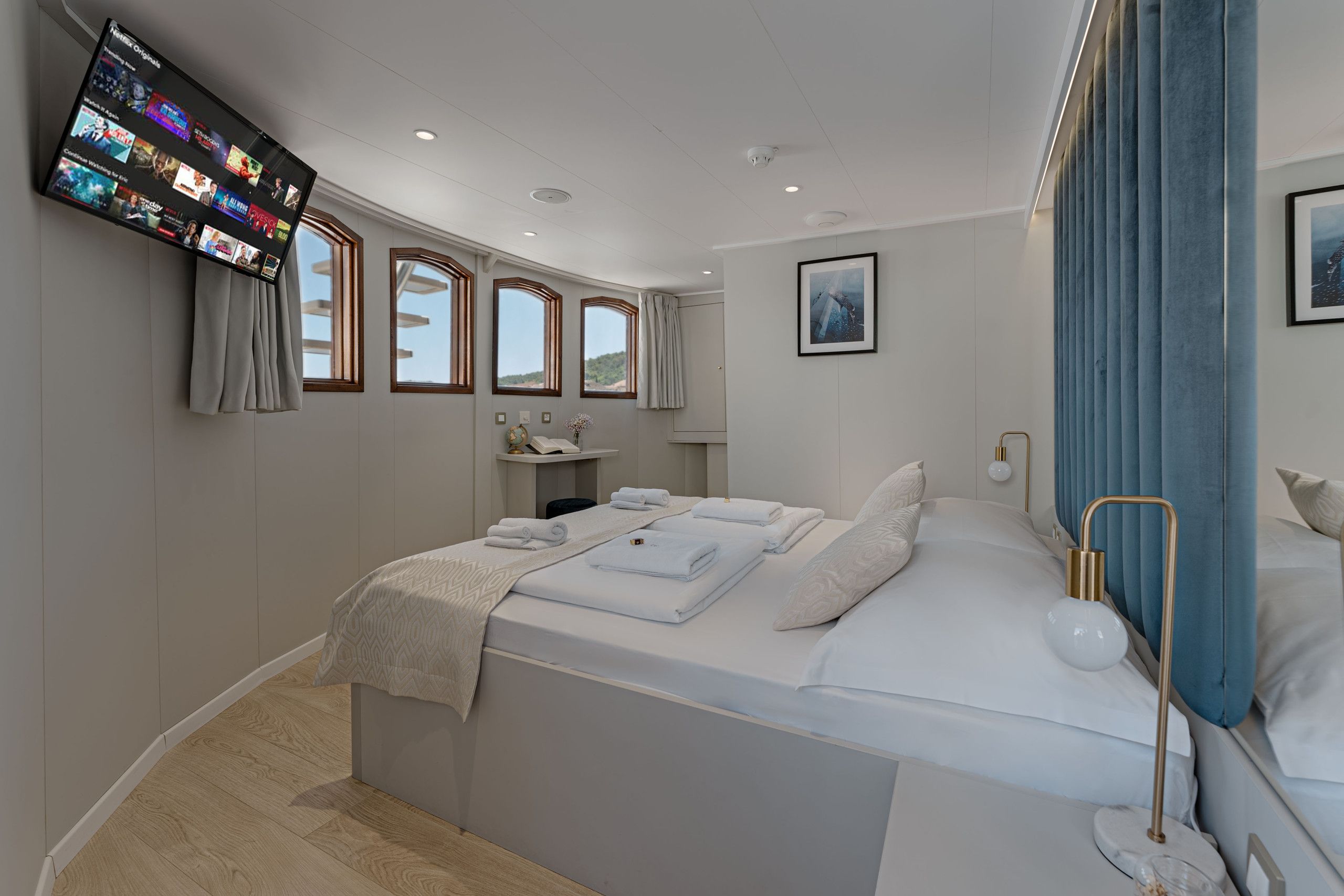 Une chambre d’hôtel moderne avec un grand lit, un téléviseur à écran plat fixé au mur, une petite table de chevet et une fenêtre avec des rideaux.
