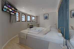 A modern hotel room with a large bed, a flat-screen TV mounted on the wall, a small bedside table, and a window with curtains.