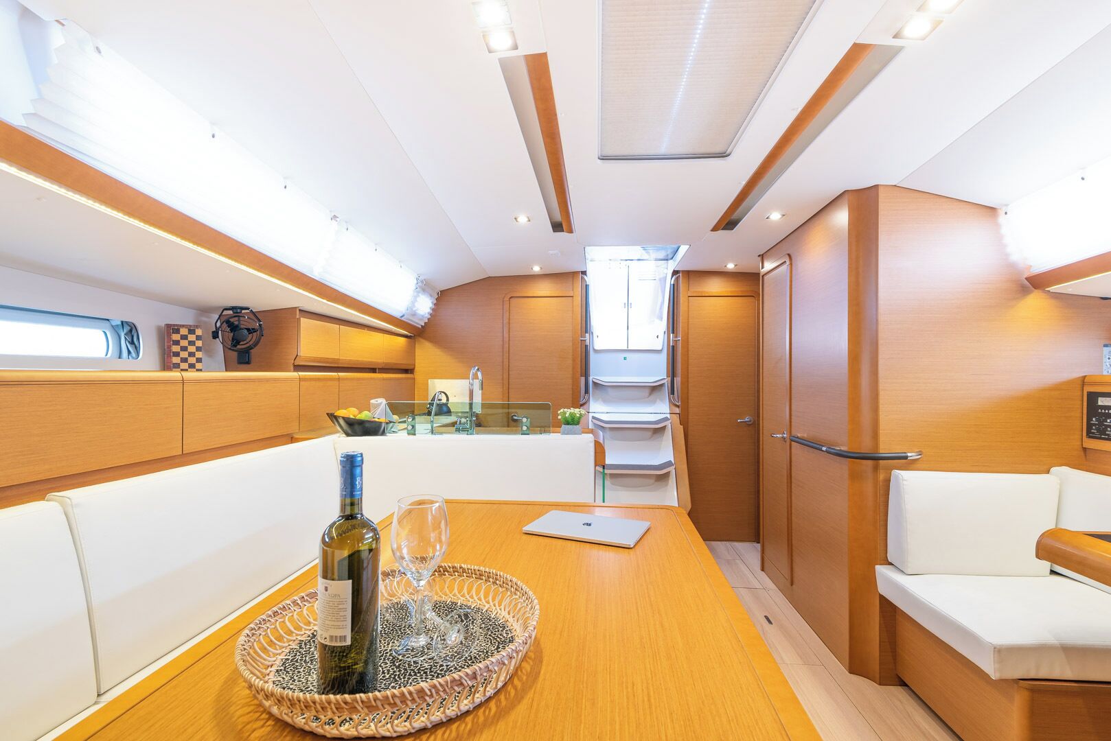 A modern interior with a wooden table, white seating, a kitchen area, and a staircase.
