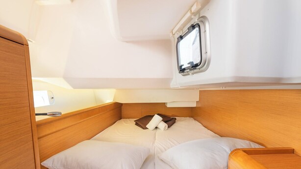 Um quarto compacto e bem iluminado com uma cama de solteiro, uma pequena janela e cabeceira de madeira.