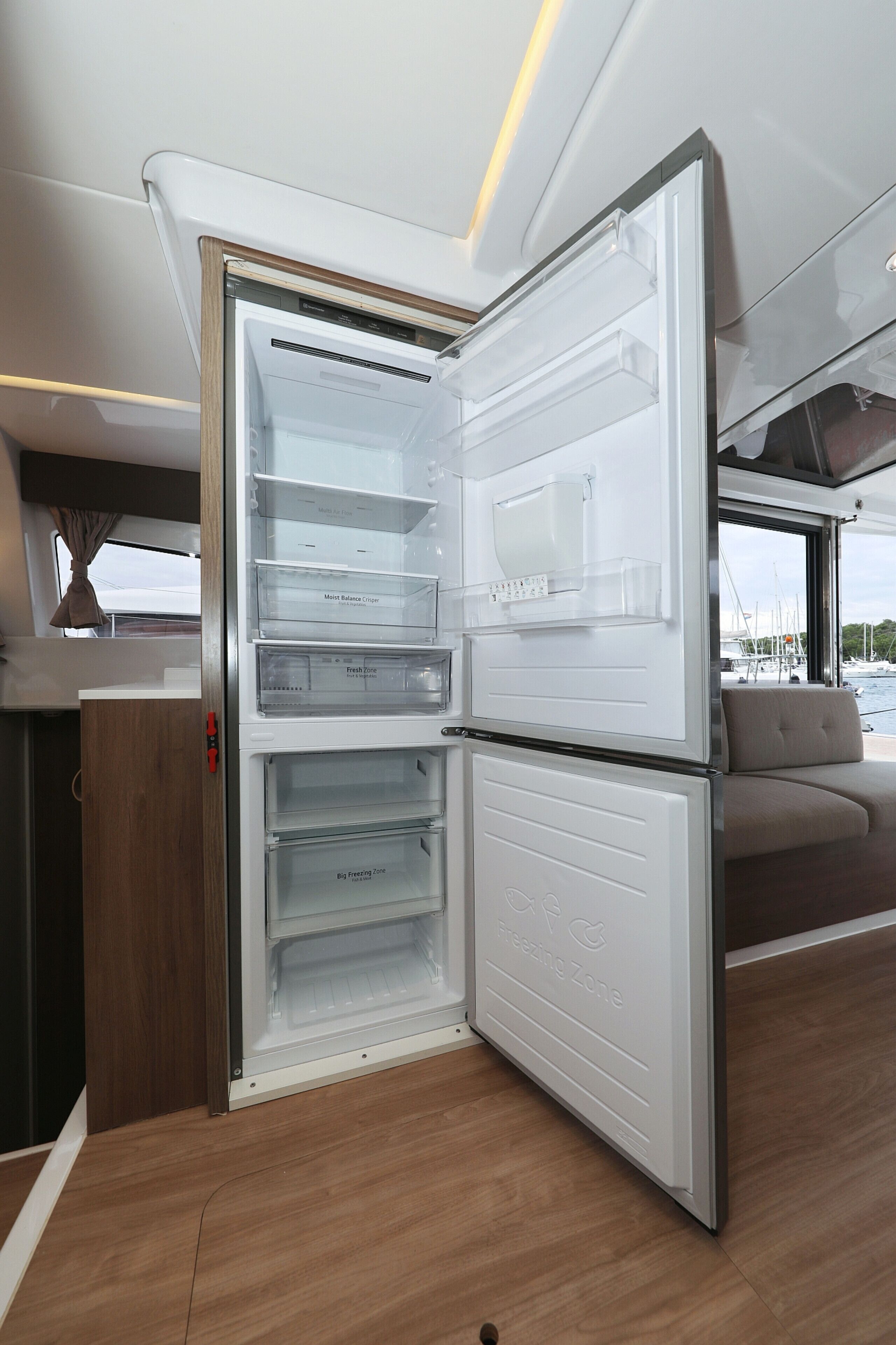 A compact kitchen with a built-in refrigerator, a wooden countertop, and a view of the marina through the window.