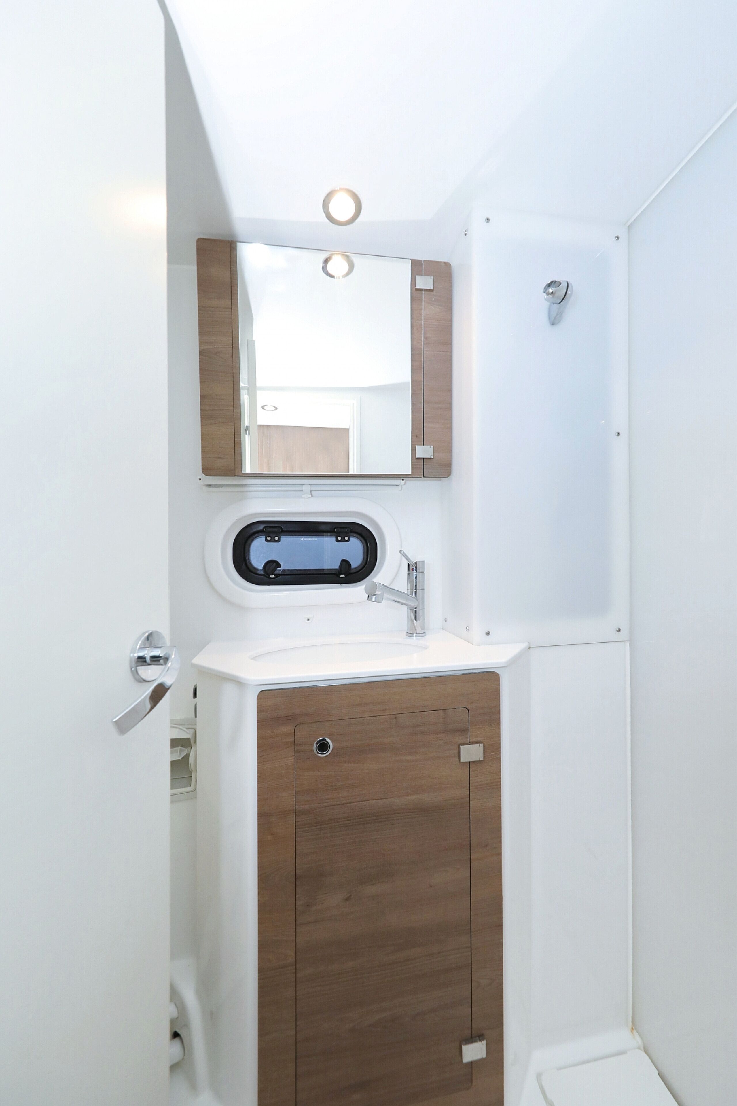Een compacte badkamer met een wit wastafel, houten opbergmeubel, een spiegel en een douche.