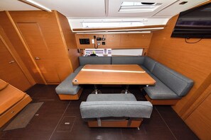Ein kompaktes Wohnmobil-Interieur mit Holztisch, grau gepolsterten Sitzen und einer Bedienkonsole.