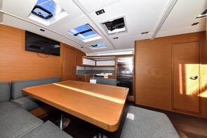 A compact interior with a dining table, cushioned seating, a kitchen area, and skylights.
