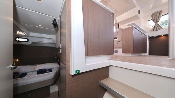 En kompakt og moderne indretning i en autocamper med seng, opbevaringsskabe og et lille siddeområde.