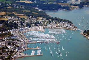 An aerial view of a coastal town with a marina filled with boats, surrounded by residential areas and a bridge connecting to the mainland.
