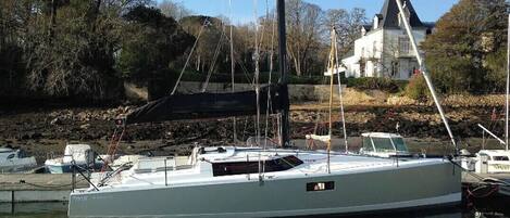 A white yacht docked at a marina with a stone wall and trees in the background.