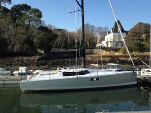 A white yacht docked at a marina with a stone wall and trees in the background.