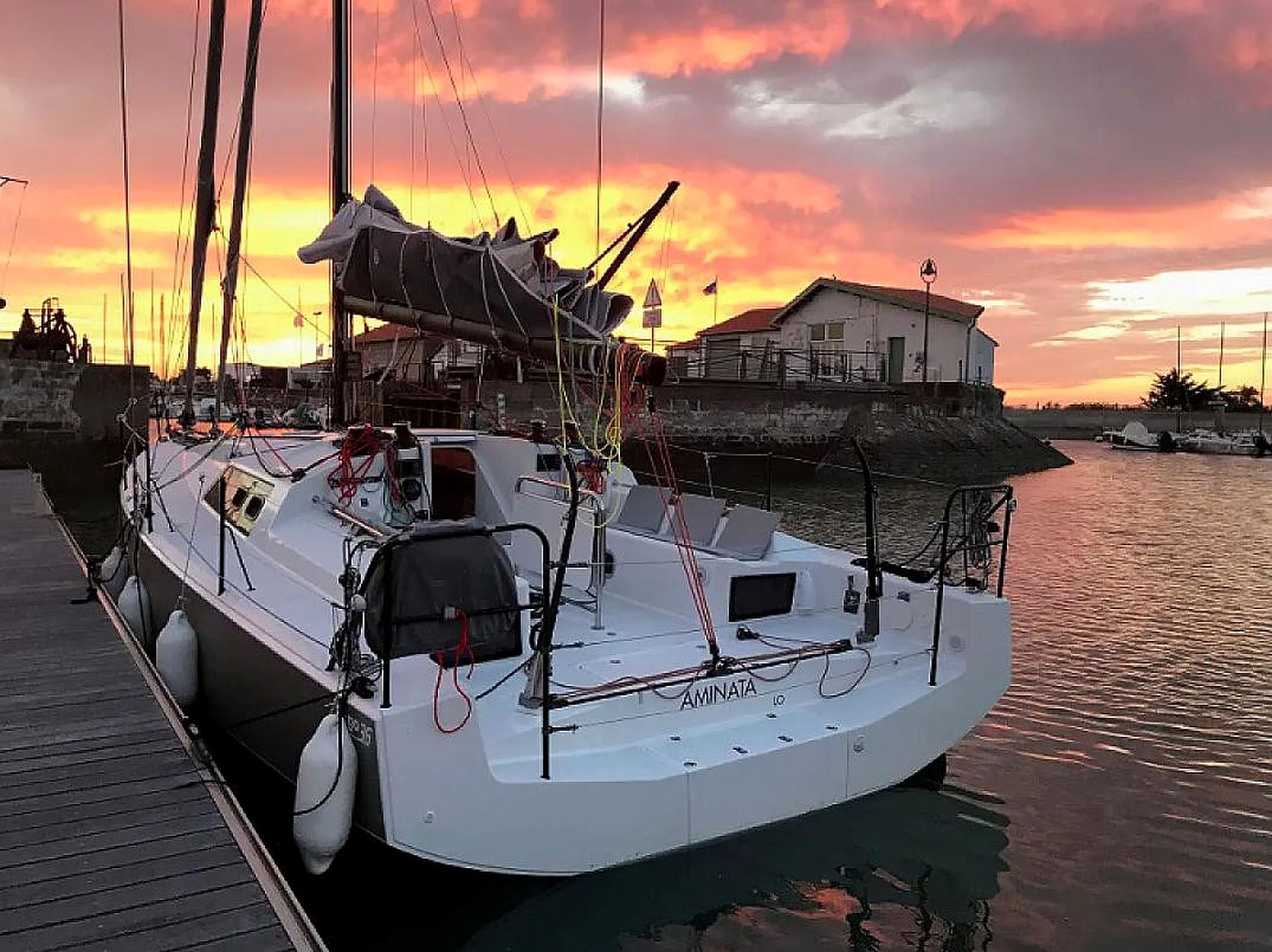A sailboat docked at a pier with a house in the background.