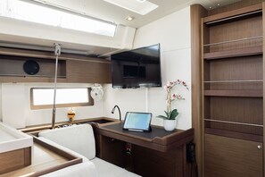 A compact, modern interior with a flat-screen TV mounted above a wooden counter, a laptop on the counter, and a small potted plant. - Sun-Kissed Sailing Adventure in the Dodecanese Islands (Kos)