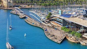 A marina with boats, a pedestrian bridge, and a building with a sloped roof. - Barcelona Sun-Kissed Sailing: A Beach Lover's Dream (Barcelona)