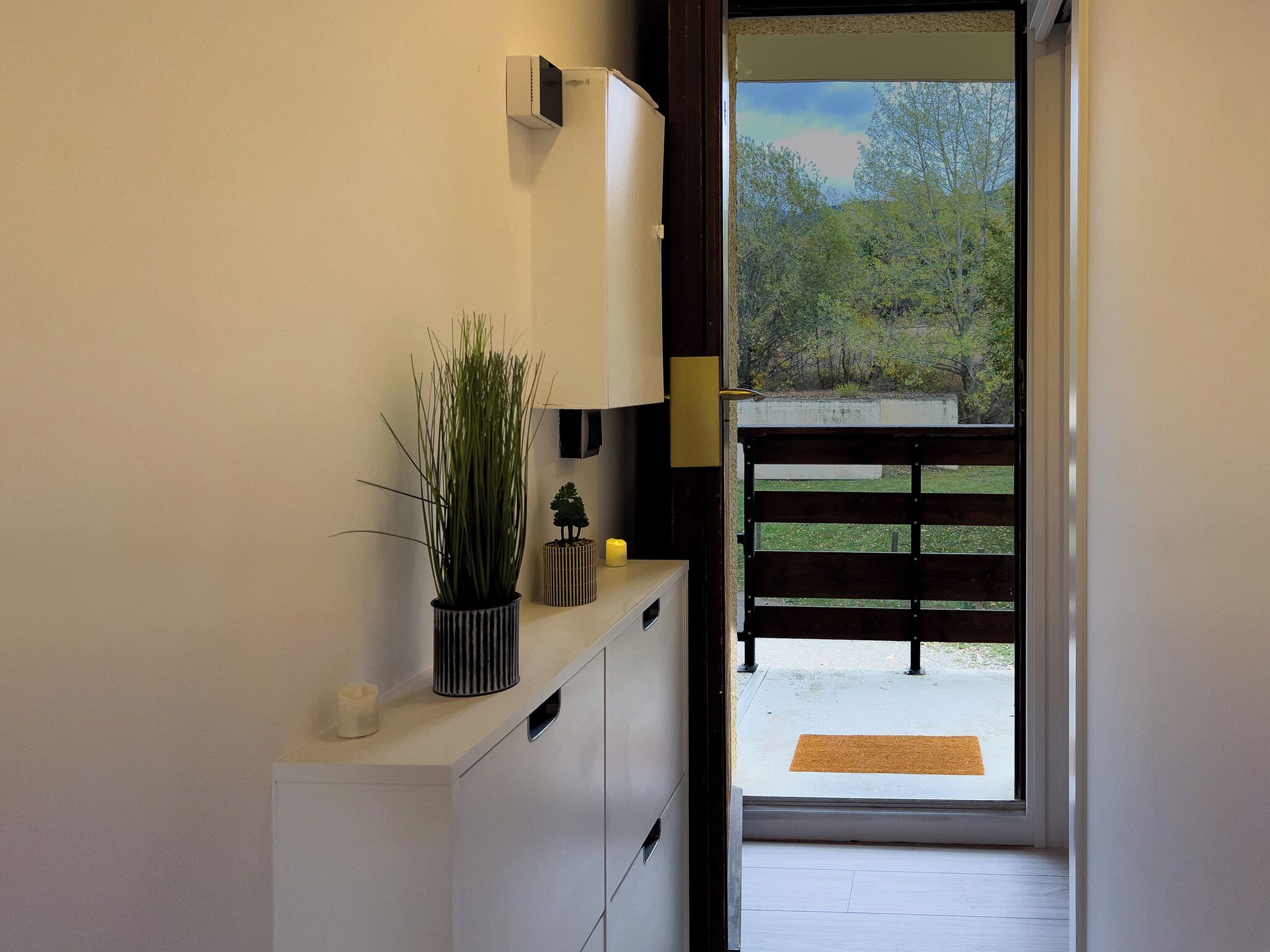 A hallway with a potted plant, a small tree, and a yellow candle on a white cabinet.
