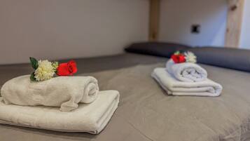 A neatly made bed with two towels, each adorned with a flower and a fruit.