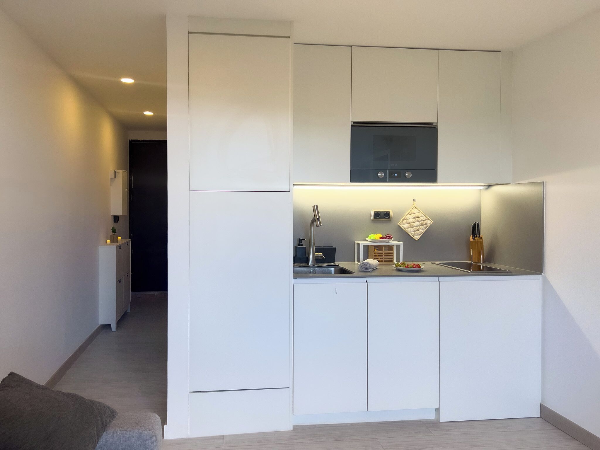 Een moderne keuken met witte kasten, een inbouwoven en een klein eiland met een spoelbak en aanrecht.