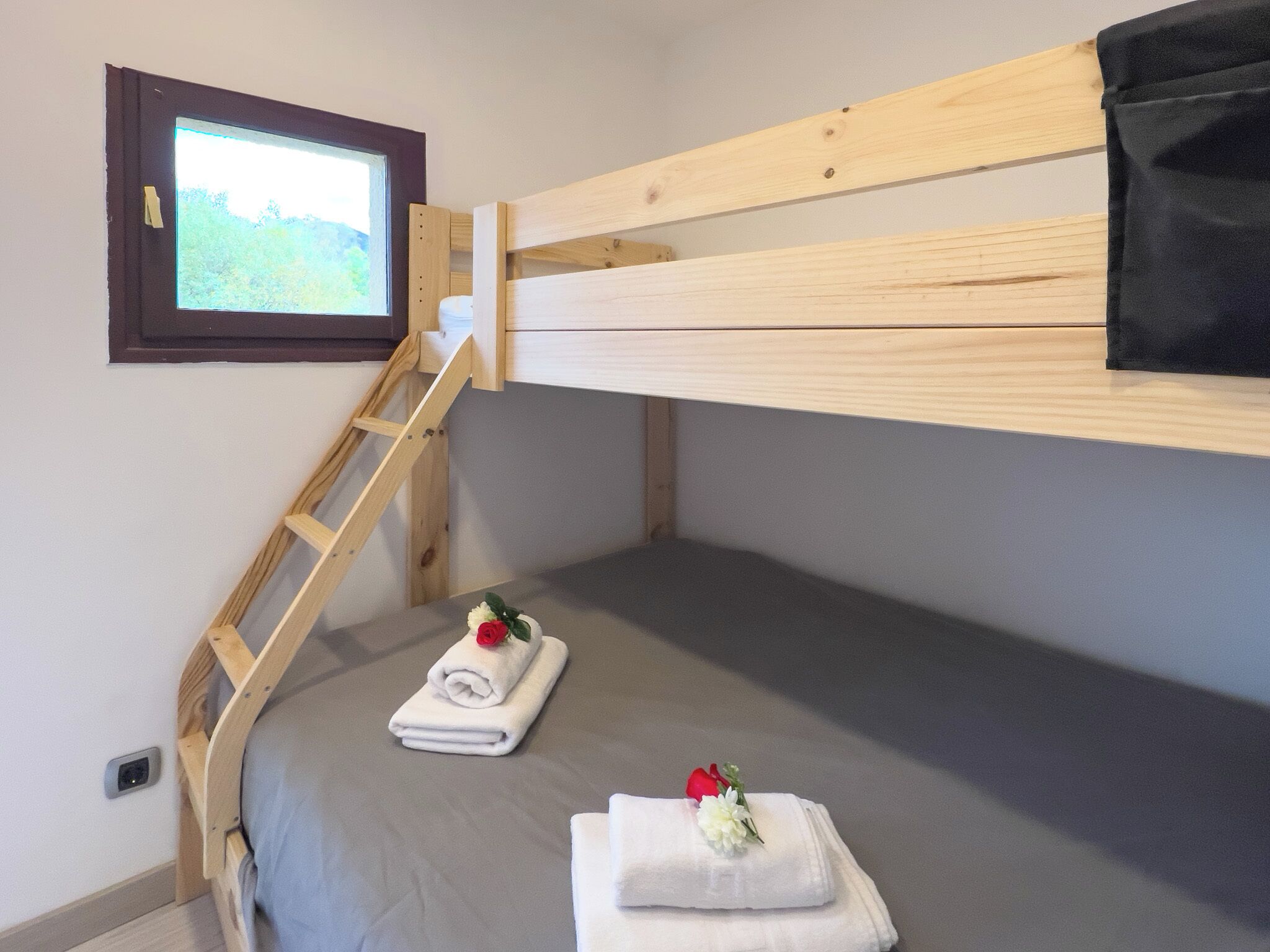 A bunk bed room with a wooden ladder, a window with a view, and towels with flowers on the bed.