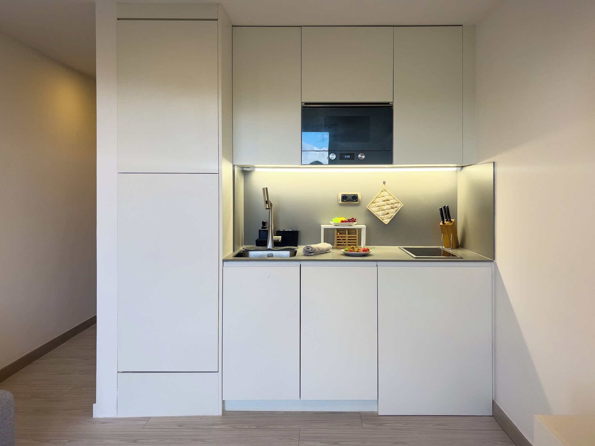 A compact kitchen with a built-in microwave, a small countertop, and a hanging pot rack.