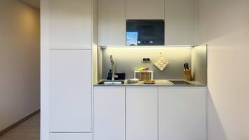 A compact kitchen with a built-in microwave, a small countertop, and a hanging pot rack.
