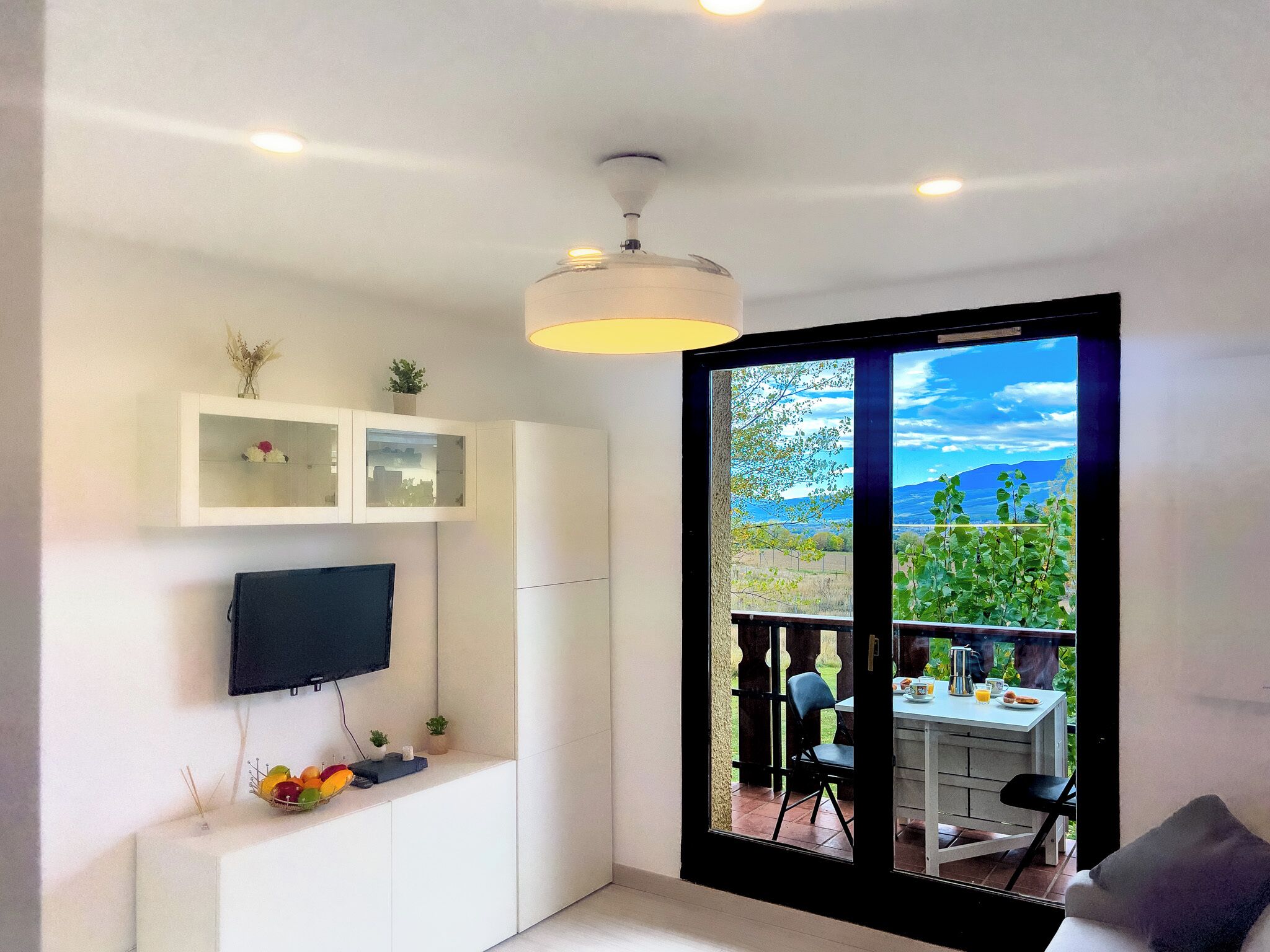 Un soggiorno moderno con una televisione a schermo piatto, un'area pranzo con tavolo e sedie, e un'ampia porta scorrevole in vetro che dà su un patio esterno.