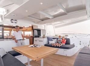 A yacht interior with a dining area, seating, and a kitchen.