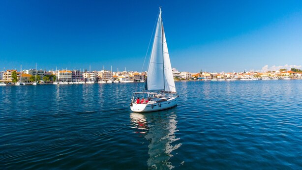 A sailboat on calm water with a cityscape in the background. - Sun-kissed Sailing Adventure in the Ionian Islands (Preveza)