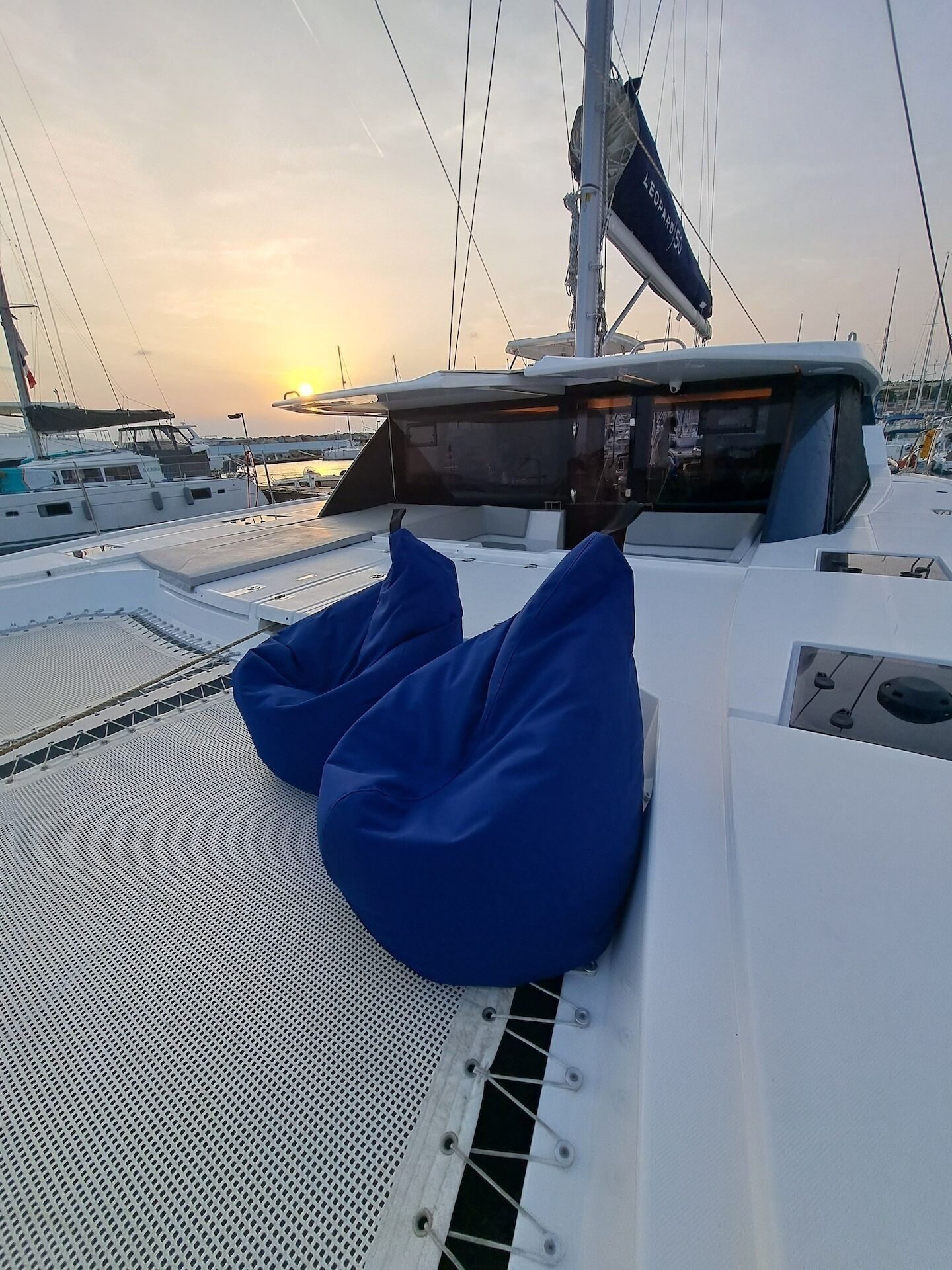 A boat deck with blue cushions, a mast, and other boats in the background.