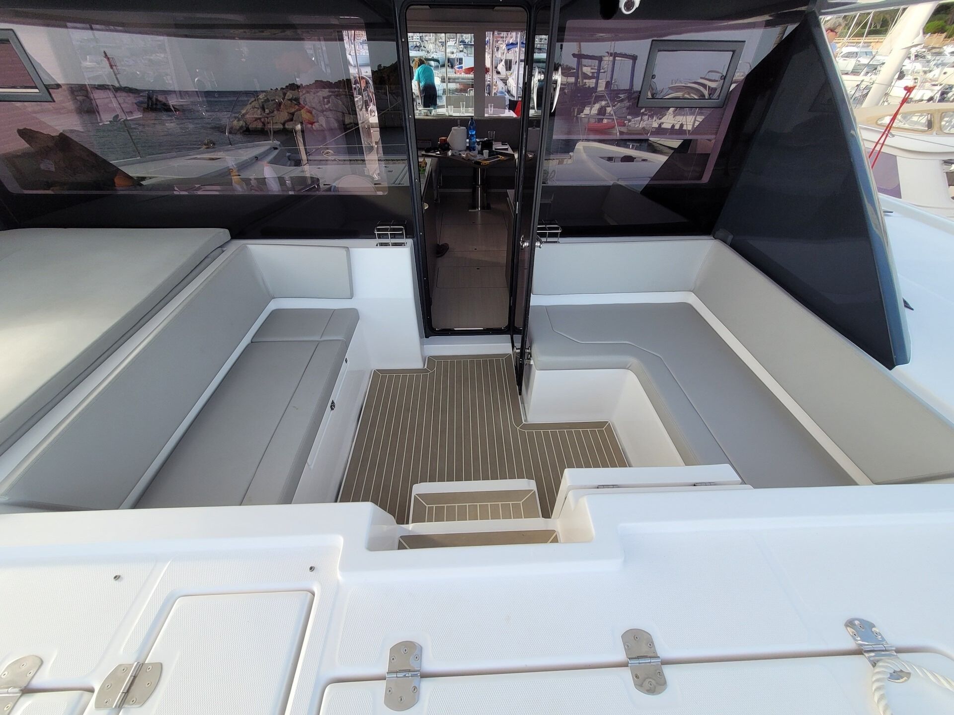Interior de un barco con un pasillo central, asientos acolchados y vista al puerto por el parabrisas.