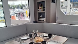 A modern dining area with a central table, cushioned seating, and a view of boats through large windows. - Sun-Kissed Sailing Adventure in Zadar, Croatia (Bibinje)